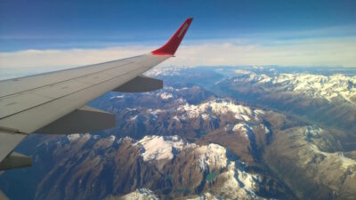 The wing of a Helvetic Airways plane flying above a snow-capped mountain range