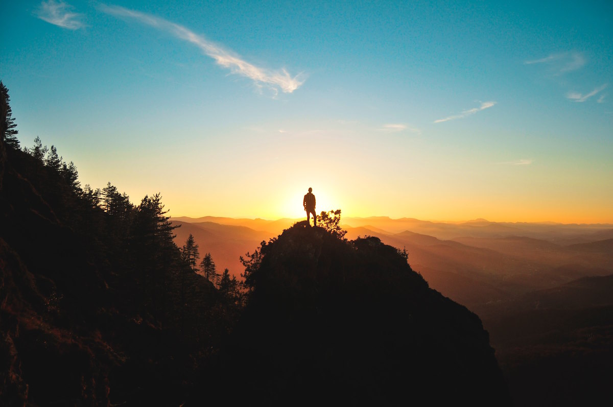 Silhouette of a man stood on top of a mountain at sunrise