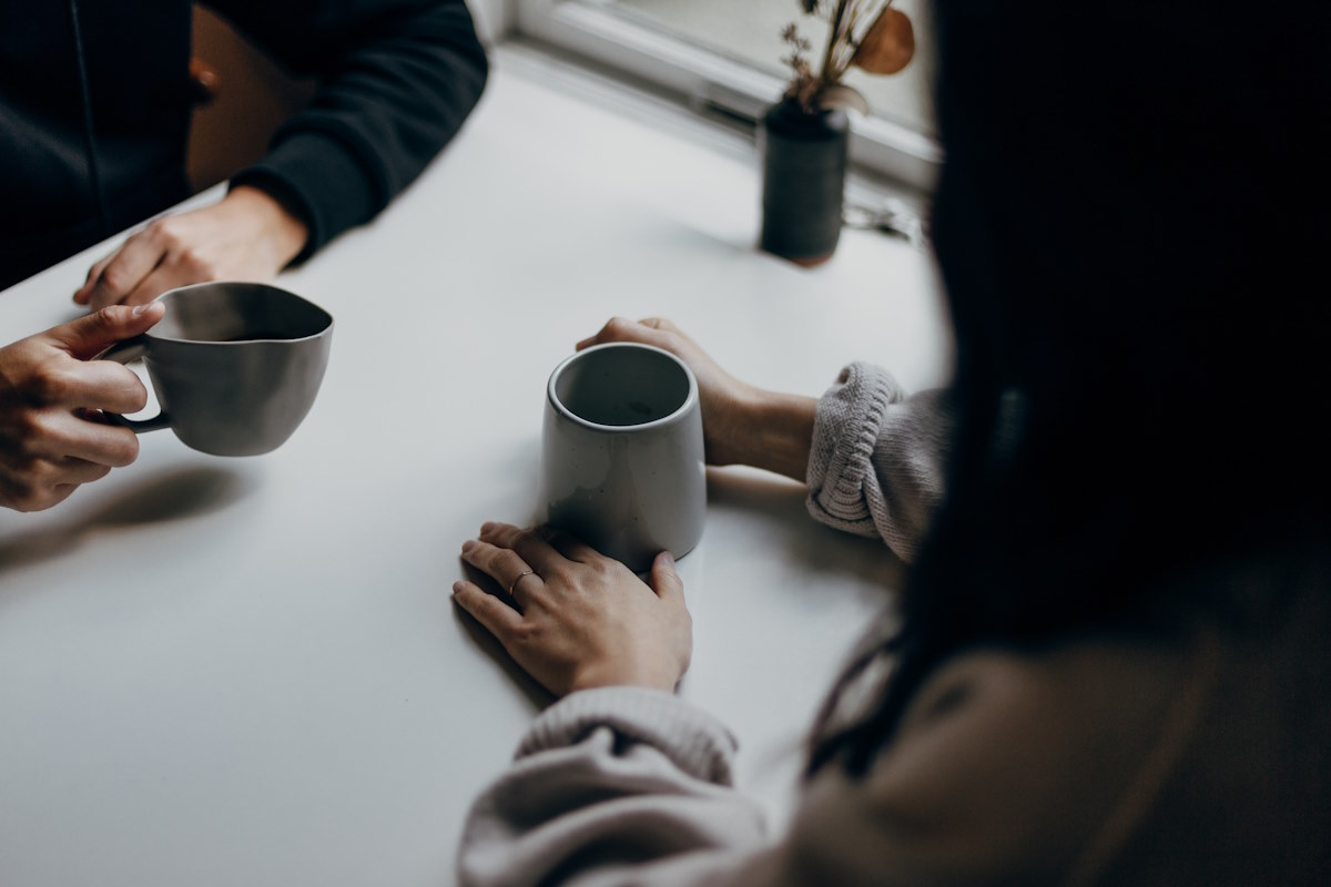 Two people sat across from each other at a table, both holding mugs