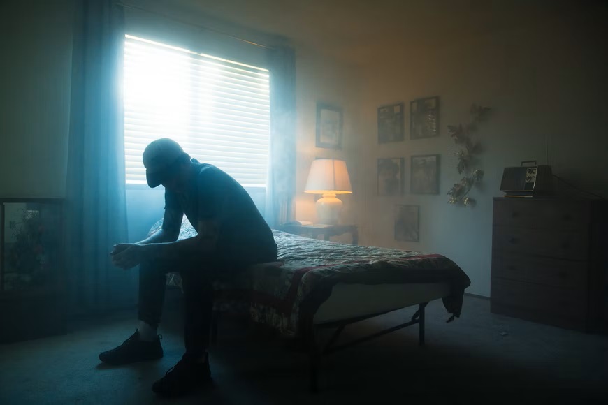 Person sat on edge of bed in dark, misty bedroom