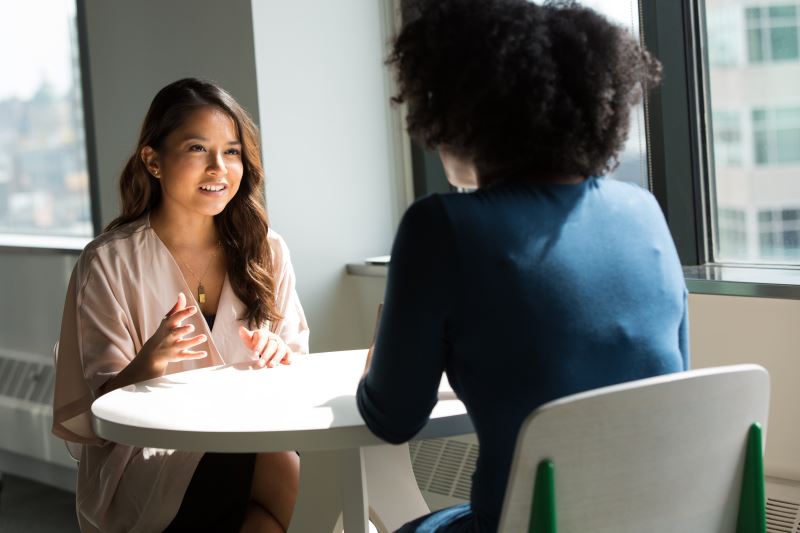 Two women talking at table near window